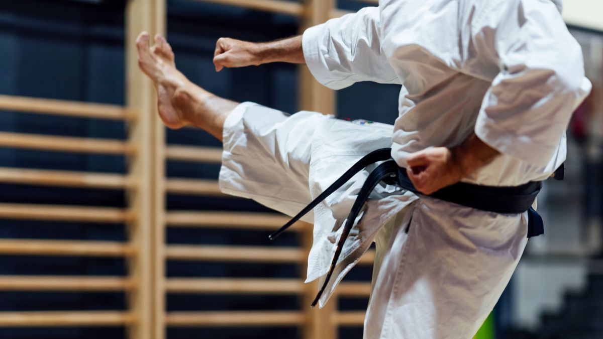 Mature man kicking while practicing karate in class