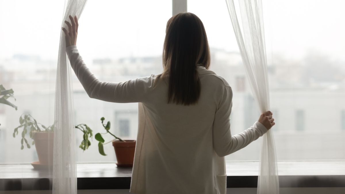 Rear,View,Woman,Stand,Near,Window,In,Living,Room,Open