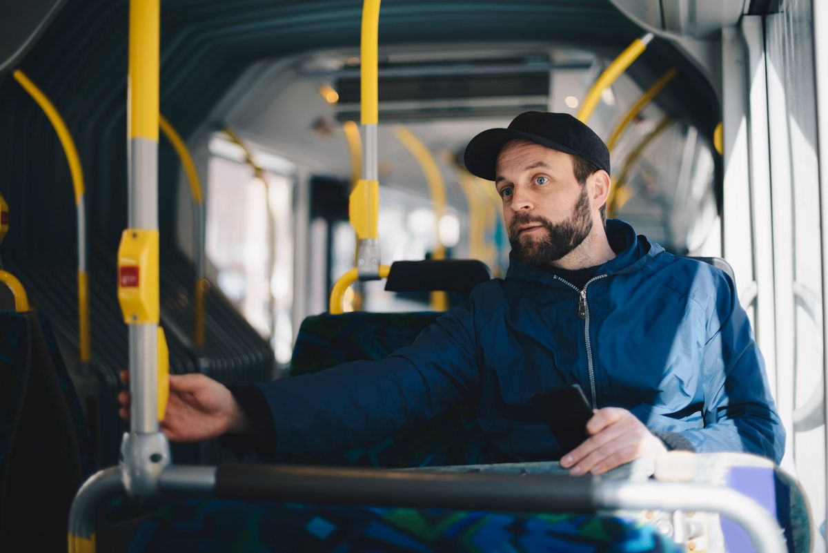 Mid adult man holding mobile phone while sitting in bus on sunny day